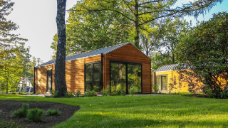 Wellness Lodge bij De Hooge Veluwe in Nederland, omgeven door bomen en groen gras op een zonnige dag.