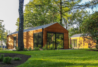 Wellness Lodge a De Hooge Veluwe, Paesi Bassi, circondata da alberi e prato verde in una giornata di sole.