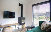 Stue i Wellness Lodge ved De Hooge Veluwe, Holland, med grøn sofa, tv og sort brændeovn.