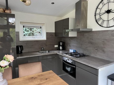 Cocina moderna en la lodge L-Pavilion 6 en De Achterhoek, Países Bajos, con gabinetes grises y gran reloj.