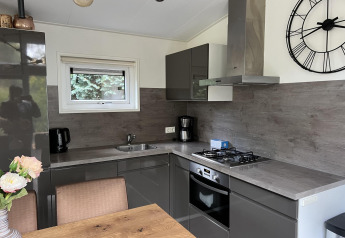 Moderne keuken in lodge L-Pavilion 6 te De Achterhoek, Nederland, met grijze kasten en grote wandklok.