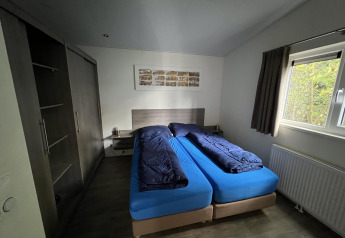 Schlafzimmer in L-Pavilion 6, De Achterhoek, Niederlande – zwei Einzelbetten, Kleiderschrank, Fenster mit Vorhang.