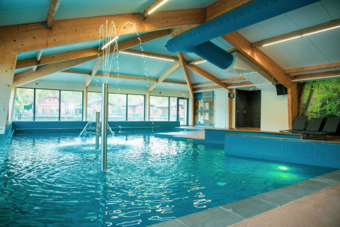 Moderner Innenpool mit Holzträgern, Wasserspielen und Liegestühlen in einer Glamping-Unterkunft.
