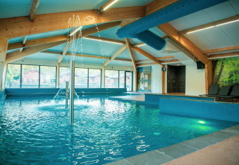 Piscina coperta con giochi d'acqua, travi in legno e lettini in una struttura di glamping.