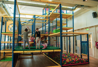 Bambini giocano in un’area giochi al coperto con vasca di palline e struttura da arrampicata in un glamping.