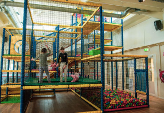 Bambini giocano in un’area giochi al coperto con vasca di palline e struttura da arrampicata in un glamping.