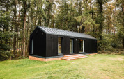 Lodge en bois noir Koya Tiny Cabin entouré de forêt à Wilsumer Berge, Allemagne, avec pelouse verte devant.