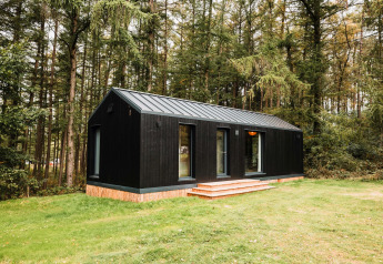 Lodge en bois noir Koya Tiny Cabin entouré de forêt à Wilsumer Berge, Allemagne, avec pelouse verte devant.