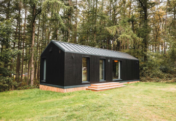 Sort træhytte kaldet Koya Tiny Cabin omgivet af skov ved Wilsumer Berge i Tyskland med grøn græsplæne.