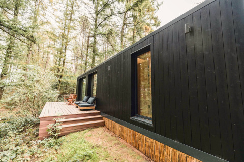 Zwarte Koya Tiny Cabin op Wilsumer Berge in Duitsland, met terras en zitplaatsen in een bosrijke omgeving.