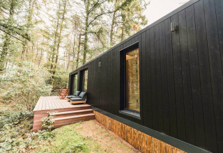 Zwarte Koya Tiny Cabin op Wilsumer Berge in Duitsland, met terras en zitplaatsen in een bosrijke omgeving.