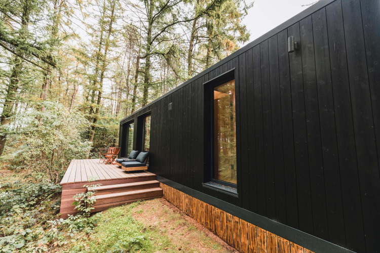 Zwarte Koya Tiny Cabin bij Wilsumer Berge in Duitsland, met houten terras en zitplaatsen in het bos.