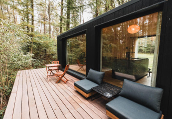 Holzterrasse am Koya Tiny Cabin im Wilsumer Berge, Deutschland, umgeben von dichtem Wald.
