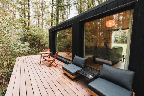 Outdoor wooden deck at Koya Tiny Cabin in Wilsumer Berge, Germany, surrounded by lush forest trees.
