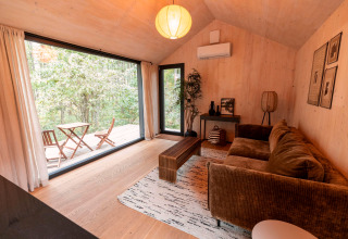Moderne woonkamer in Koya Tiny Cabin met grote ramen, bruine zetel en boszicht in Wilsumer Berge, Duitsland.