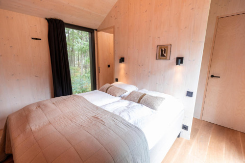 Dormitorio en Koya Tiny Cabin en Wilsumer Berge, Alemania, con cama doble y gran ventana con vista al bosque.