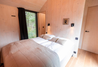 Dormitorio en Koya Tiny Cabin en Wilsumer Berge, Alemania, con cama doble y gran ventana con vista al bosque.