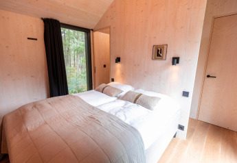 Soveværelse i Koya Tiny Cabin på Wilsumer Berge, Tyskland, med dobbeltseng og store vinduer mod skoven.