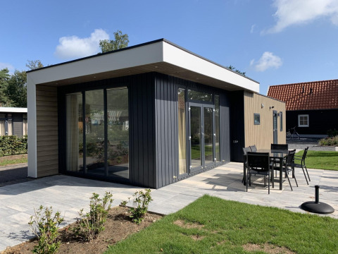 Lodge moderno Pavilion 6 en De Achterhoek, Países Bajos, terraza con comedor exterior y césped verde.