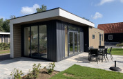 Lodge moderno Pavilion 6 en De Achterhoek, Países Bajos, terraza con comedor exterior y césped verde.