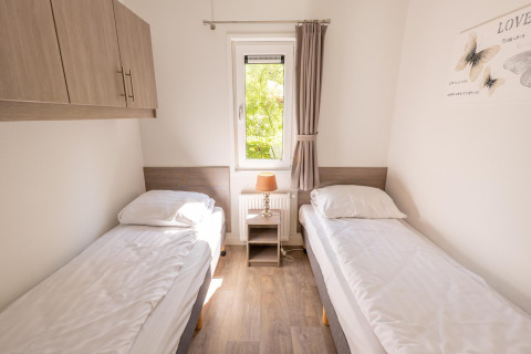 Helles Schlafzimmer mit zwei Einzelbetten, Fenster und Nachttischlampe in Pavilion 6 in De Achterhoek, Niederlande.