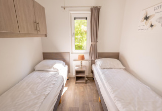 Luminoso dormitorio doble con dos camas individuales, ventana y lámpara en Pavilion 6 en De Achterhoek, Holanda.