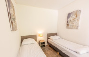 Lichte kamer met twee aparte bedden, nachtkastje, lamp en wanddecoratie in Pavilion 6, De Achterhoek, Nederland.