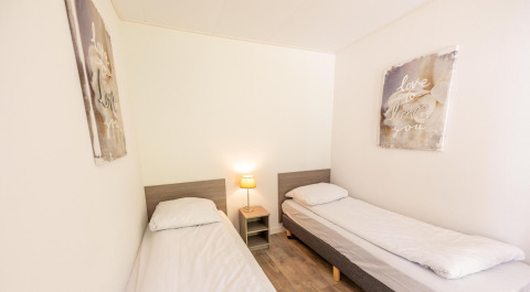 Lichte kamer met twee aparte bedden, nachtkastje, lamp en wanddecoratie in Pavilion 6, De Achterhoek, Nederland.