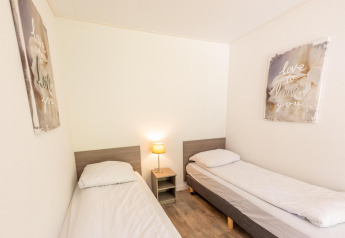 Lichte kamer met twee aparte bedden, nachtkastje, lamp en wanddecoratie in Pavilion 6, De Achterhoek, Nederland.