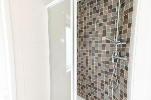 Ducha moderna en el Pavilion 6 de De Achterhoek, Países Bajos, con azulejos marrones y puerta de cristal.