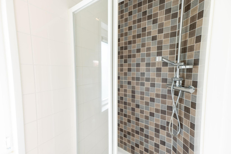 Modern shower in Pavilion 6 at De Achterhoek, Netherlands, with brown mosaic tiles and a glass door.