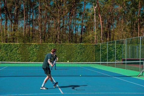 Hombre jugando tenis en un día soleado en Pavilion 6, De Achterhoek, Países Bajos, rodeado de vegetación.
