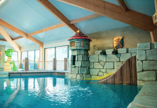 Piscina cubierta con decoración de castillo y tobogán en un alojamiento glamping ideal para familias.