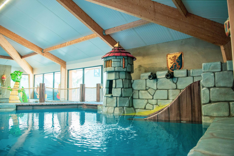 Indoor swimming pool with castle-themed decor and slide at a glamping accommodation for families.