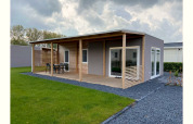 Foto van Cottage 4 lodge in De Biesbosch, Nederland, met houten terras, tuinset en groene gazonstrook.