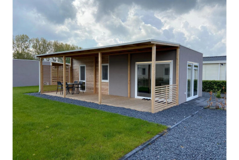 Foto del Lodge Cottage 4 en De Biesbosch, Países Bajos, con terraza de madera y césped verde al aire libre.