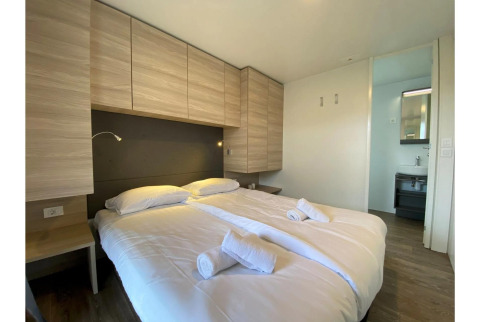 Dormitorio moderno con cama doble, sábanas limpias, toallas y armarios de madera en Cottage 4, De Biesbosch.