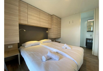 Moderne slaapkamer met tweepersoonsbed, fris beddengoed, handdoeken en houten kasten in Cottage 4, De Biesbosch.