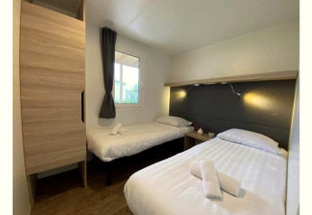Slaapkamer in Cottage 4, De Biesbosch, Nederland met twee eenpersoonsbedden, raam en warme verlichting.