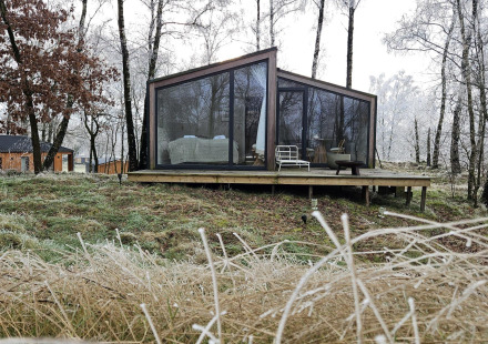 Moderne glazen hut Cabin on the Hill bij Wilsumer Berge, Duitsland, tussen kale winterbomen en gras.