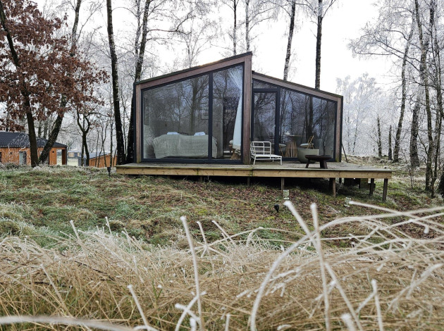Moderne glazen hut Cabin on the Hill bij Wilsumer Berge, Duitsland, tussen kale winterbomen en gras.