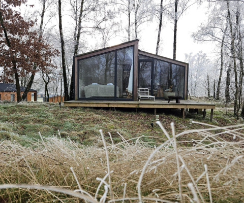 Cabane moderne vitrée Cabin on the Hill à Wilsumer Berge, Allemagne, entourée d’arbres d’hiver givrés.