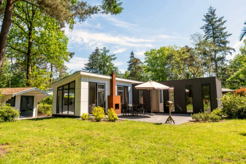 Modern L-Pavilion 6 lodge at De Biesbosch in the Netherlands with patio, umbrella, and lush greenery.