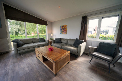Living room at L-Pavilion 6, De Biesbosch, Netherlands, with large windows, sofas, and a wooden table.