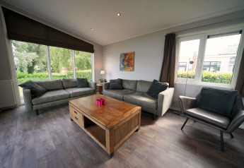 Sala de estar en L-Pavilion 6, De Biesbosch, Países Bajos, con grandes ventanas, sofás y mesa de madera.