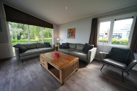 Sala de estar en L-Pavilion 6, De Biesbosch, Países Bajos, con grandes ventanas, sofás y mesa de madera.