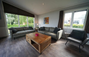 Woonkamer in L-Pavilion 6 bij De Biesbosch, Nederland, met grote ramen, banken en houten tafel.