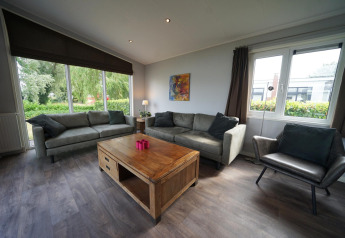 Woonkamer in L-Pavilion 6 te De Biesbosch, Nederland, met grote ramen, zitbanken en houten tafel.