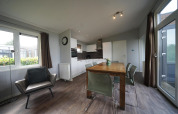 Moderne woonkamer en keuken in L-Pavilion 6 lodge bij De Biesbosch, Nederland, met eettafel en fauteuil.