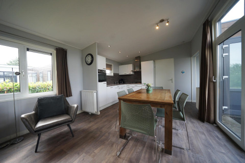 Soggiorno e cucina moderni nel lodge L-Pavilion 6 a De Biesbosch, Paesi Bassi, con tavolo e poltrona.